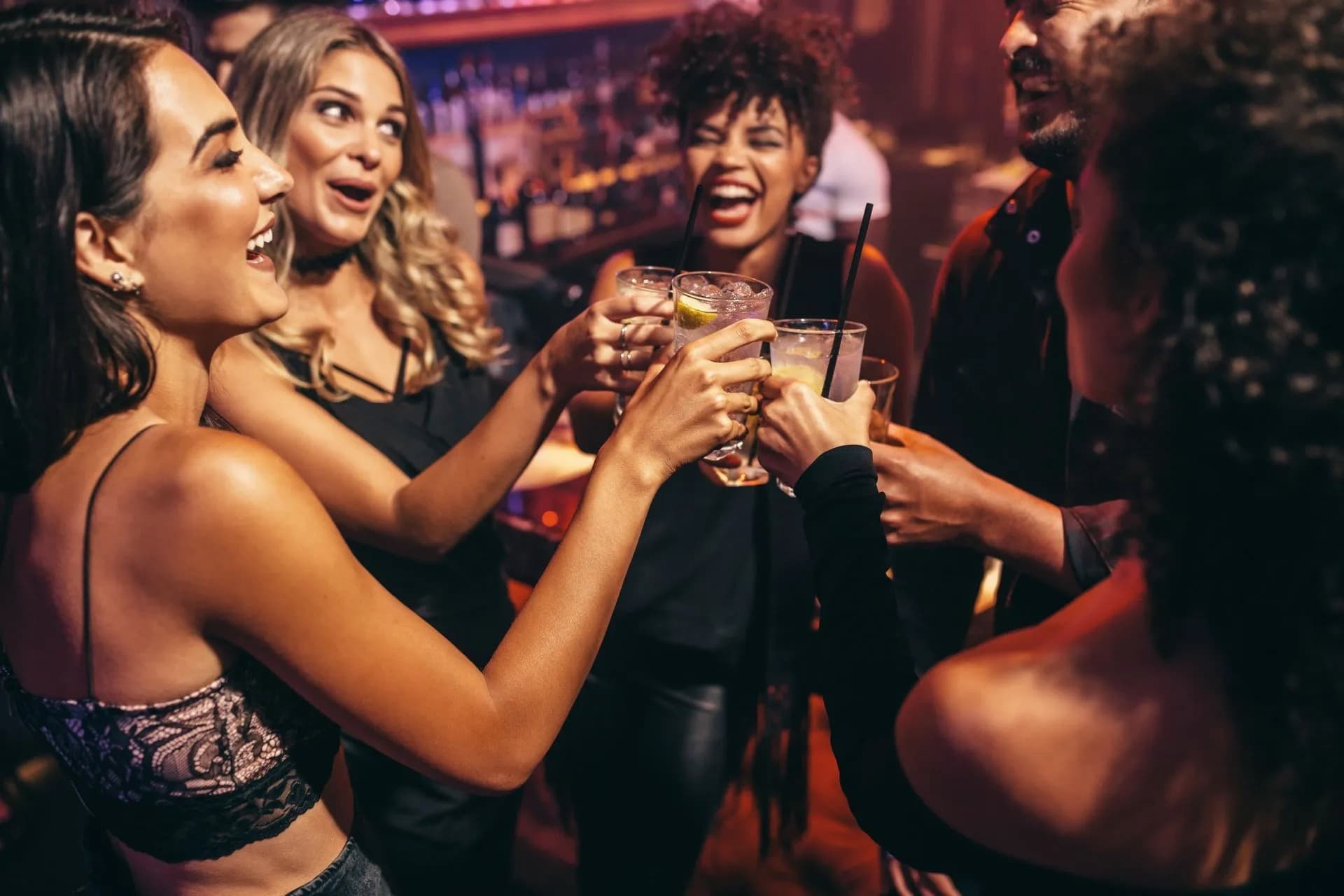 A group of friends joyfully toasting with drinks at a lively bar.