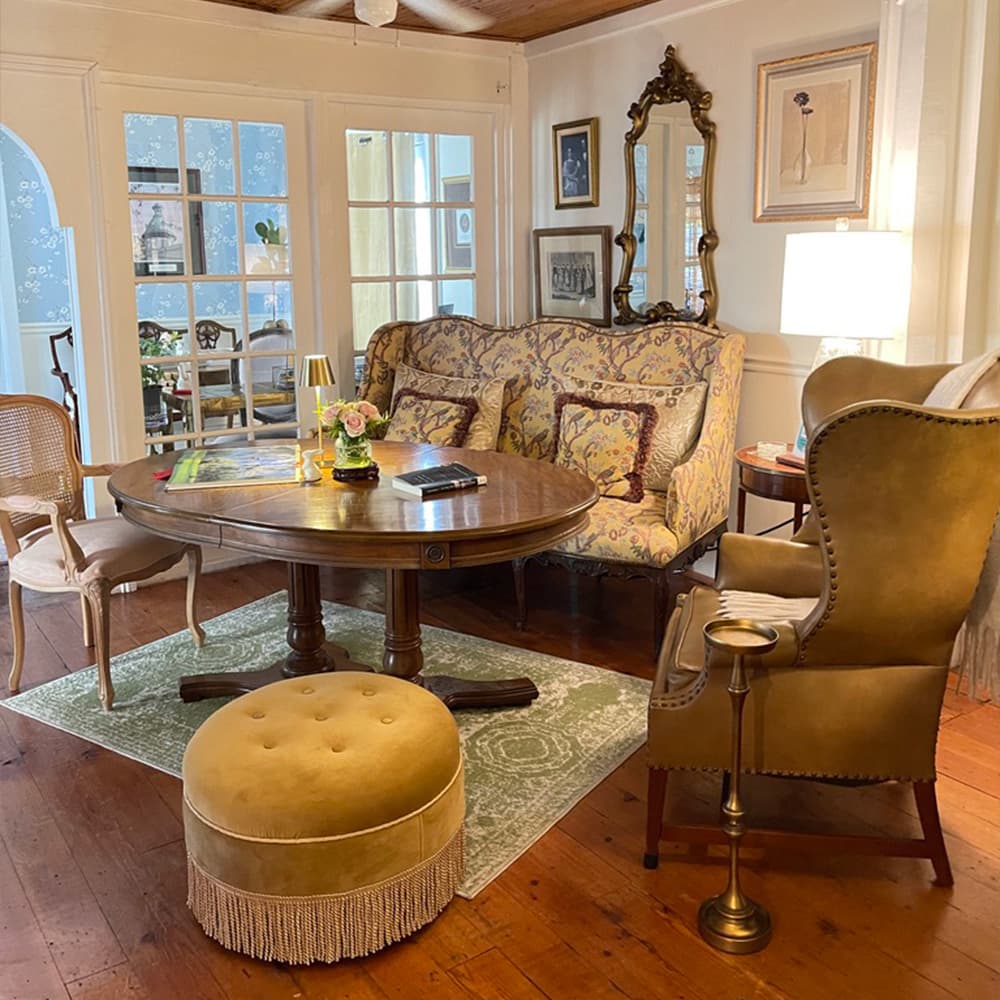 A cozy living room featuring a floral-patterned sofa, a round wooden table, and various elegant chairs with warm lighting.