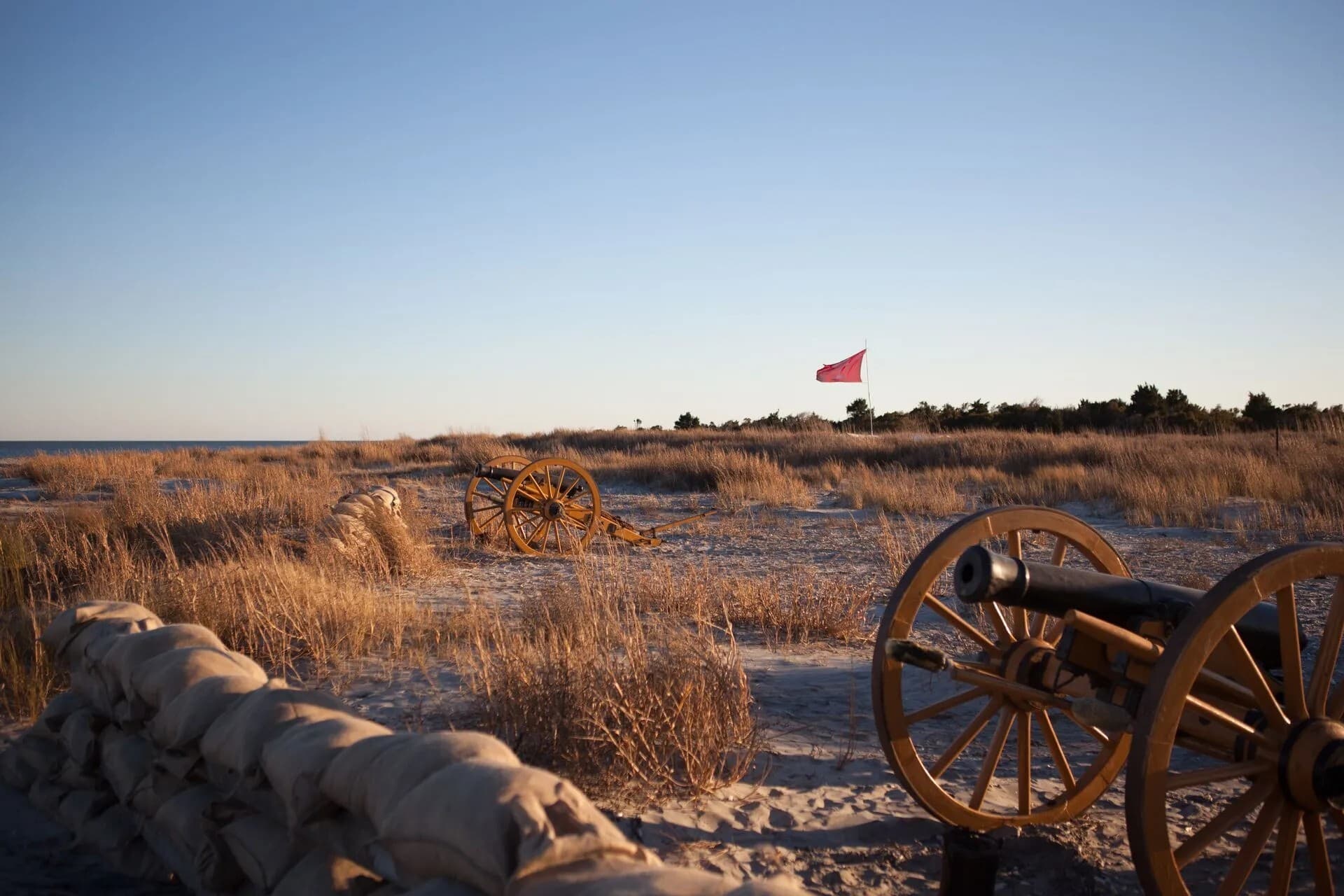 Historic cannons and a red flag on a sandy beach at sunset. Historic cannons and a red flag on a sandy beach at sunset.