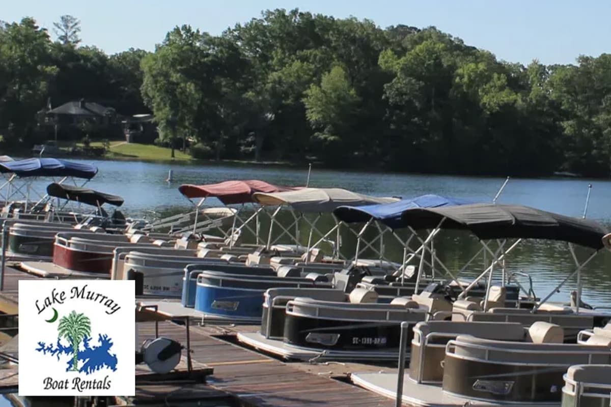 A row of rental boats lined up at Lake Murray with trees and water in the background.