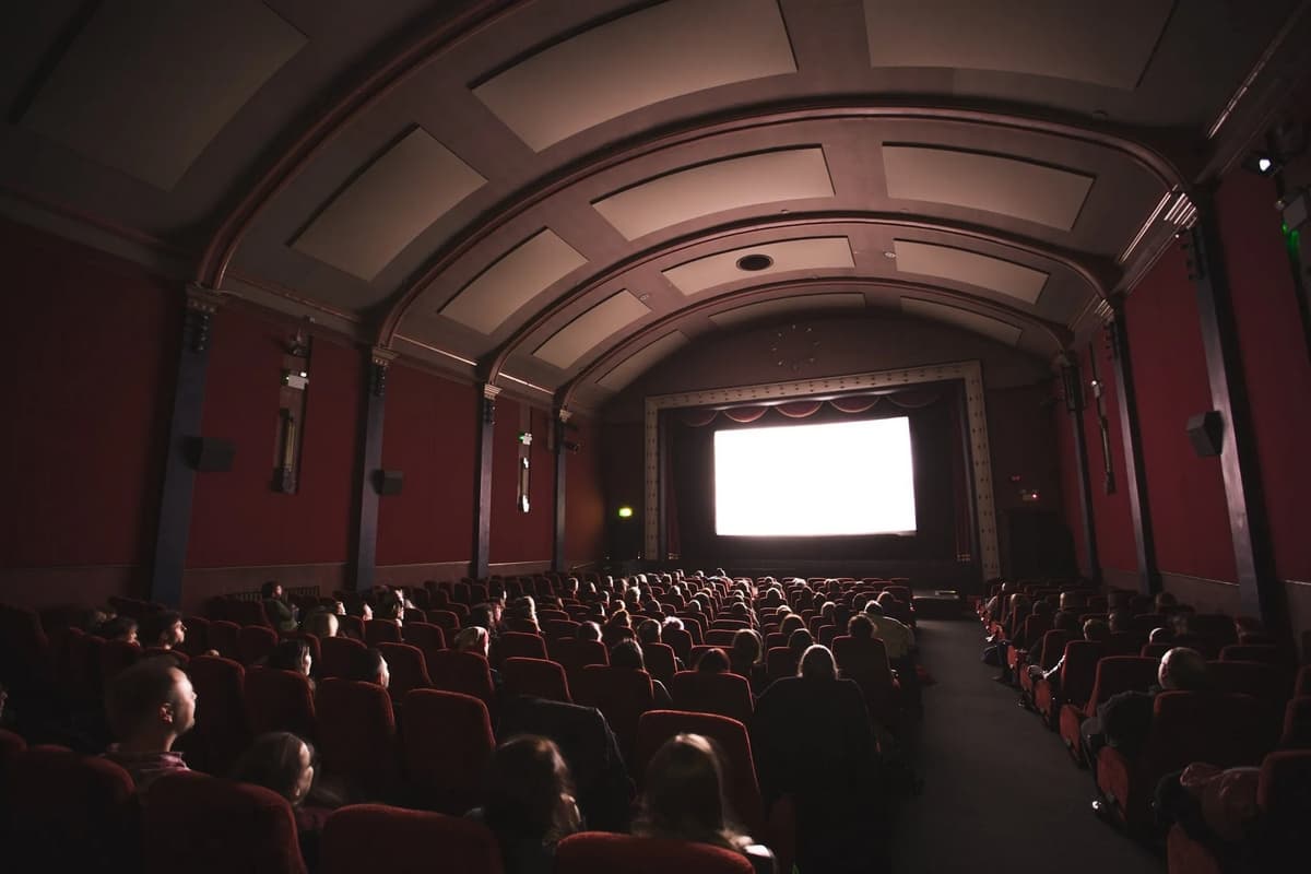 A dimly lit theater filled with people watching a movie on a large screen.
