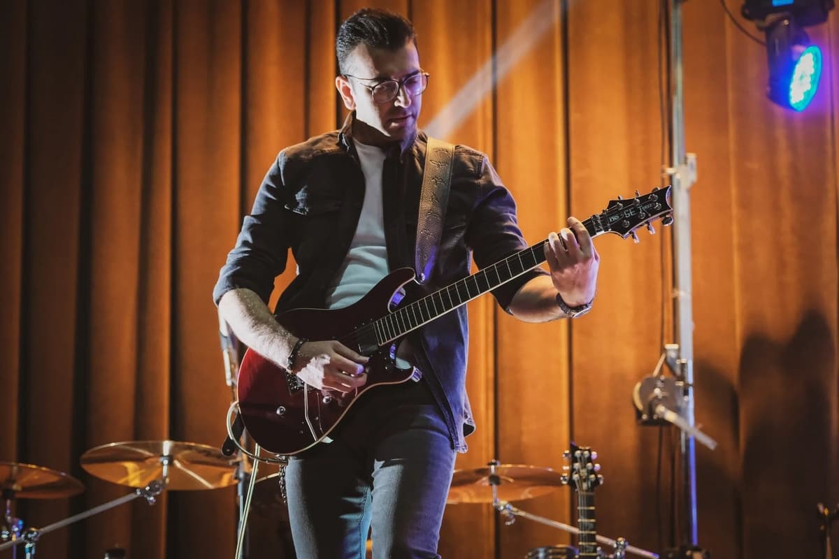 A musician playing an electric guitar on stage under dramatic lighting.