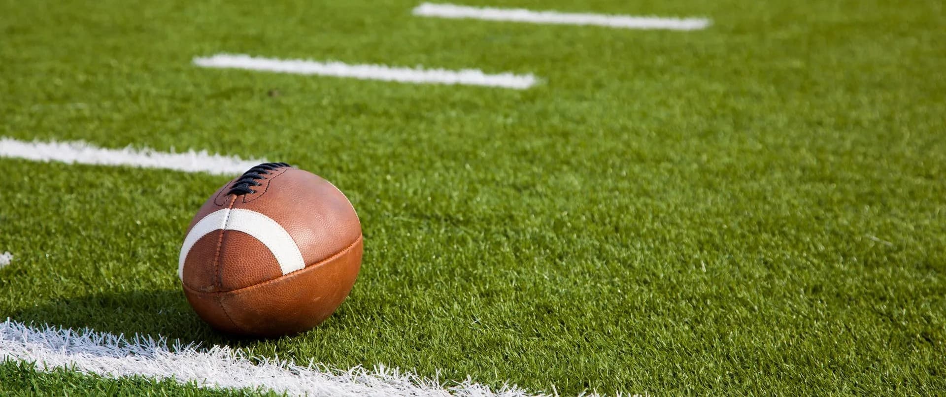 A football resting on green artificial turf marked with white lines.