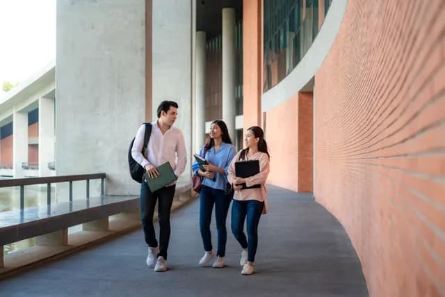 Three students walk together along a modern corridor, chatting and carrying books.