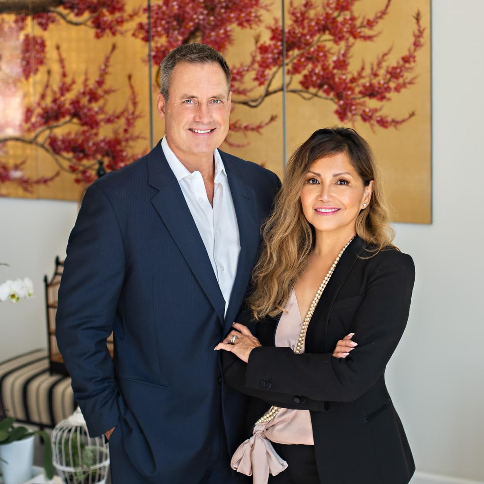 A professional couple stands together, smiling, in front of decorative artwork.