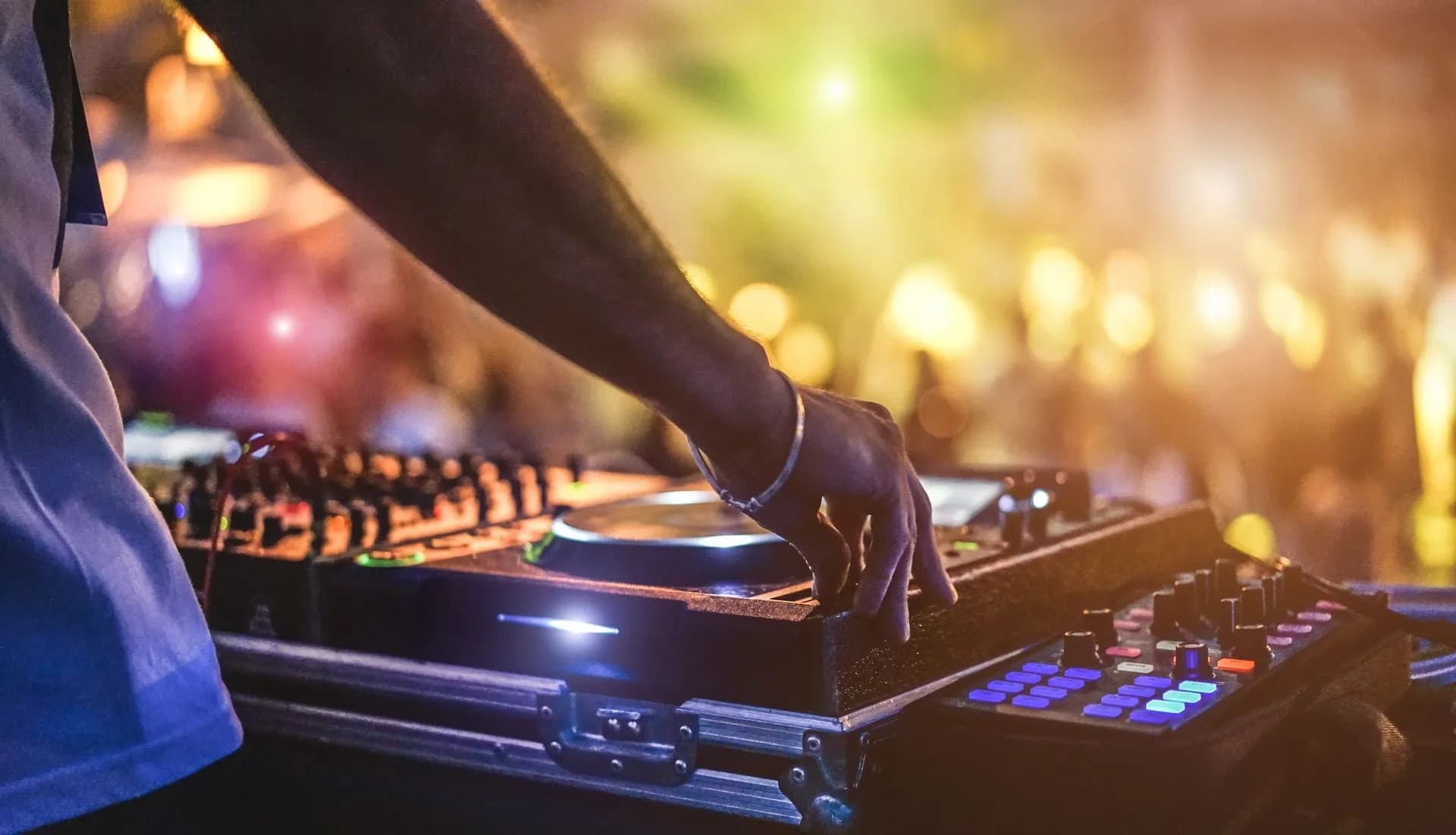 A DJ adjusts equipment during a lively performance in a colorful, illuminated venue.