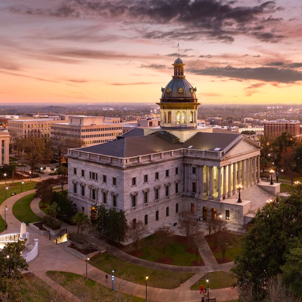Historic building with a dome at sunset surrounded by cityscape and park.