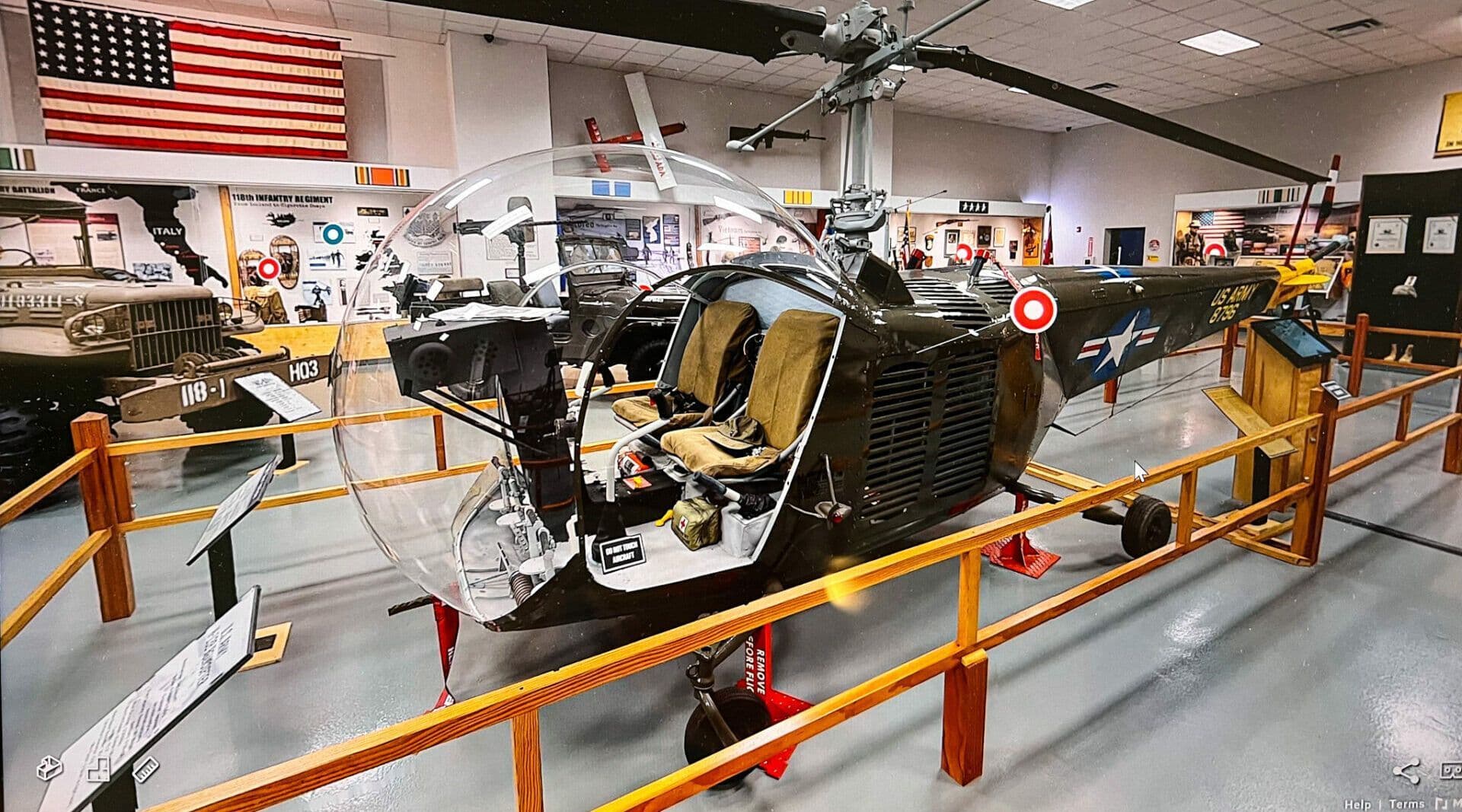 A military helicopter on display in a museum, surrounded by various military vehicles and memorabilia.