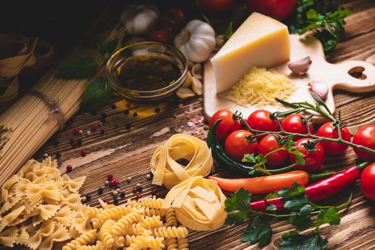 A variety of pasta, tomatoes, cheese, garlic, and herbs arranged on a wooden surface.