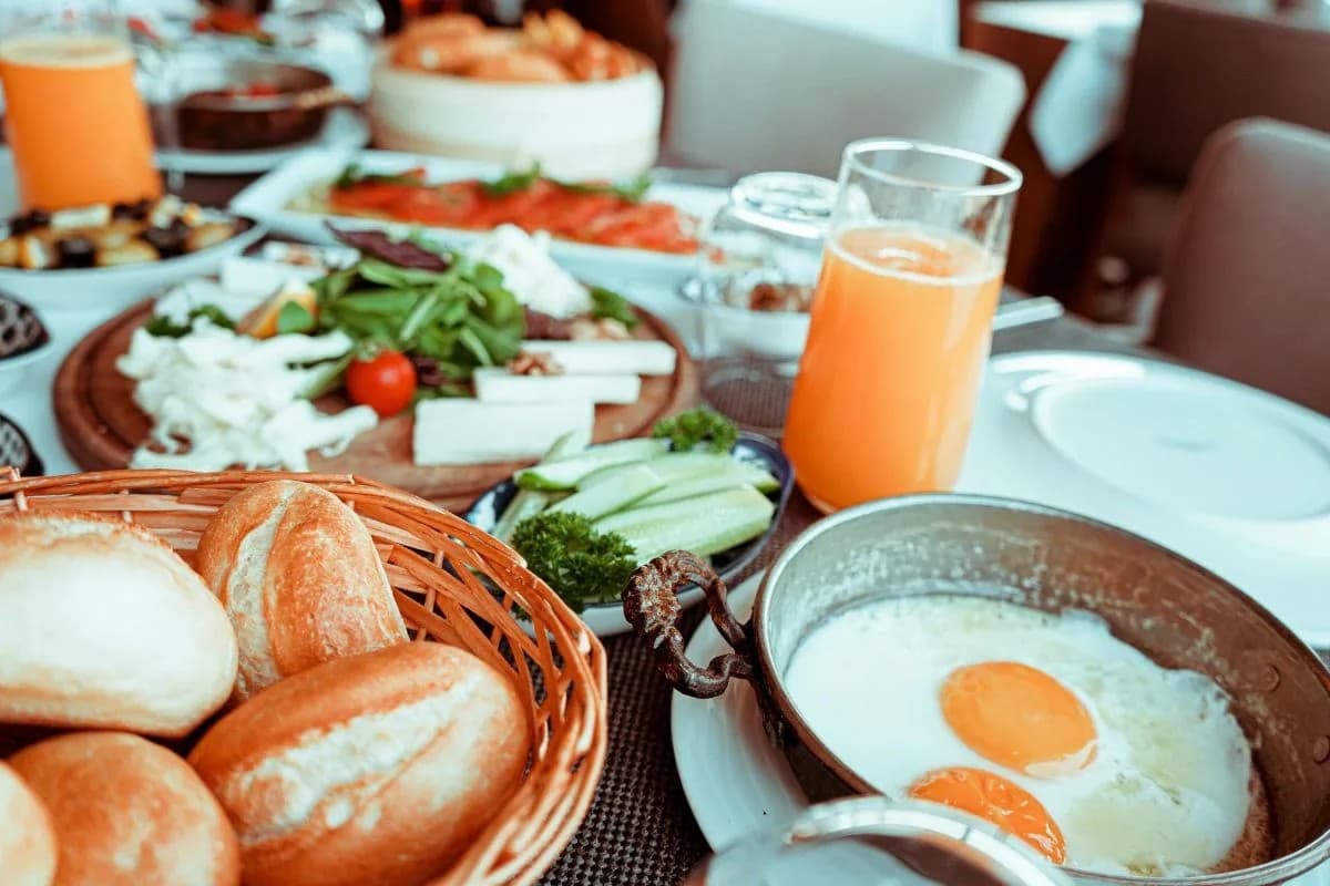 A colorful breakfast spread featuring eggs, fresh vegetables, bread rolls, and a glass of orange juice.