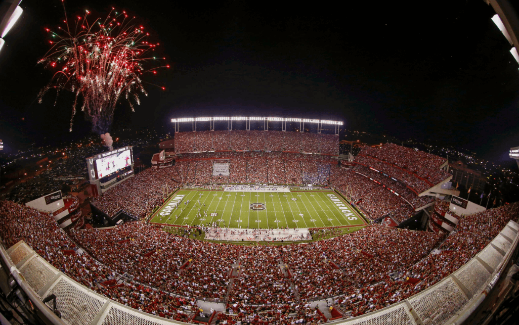 A vibrant stadium filled with fans celebrates under fireworks during a night football game. A vibrant stadium filled with fans celebrates under fireworks during a night football game.
