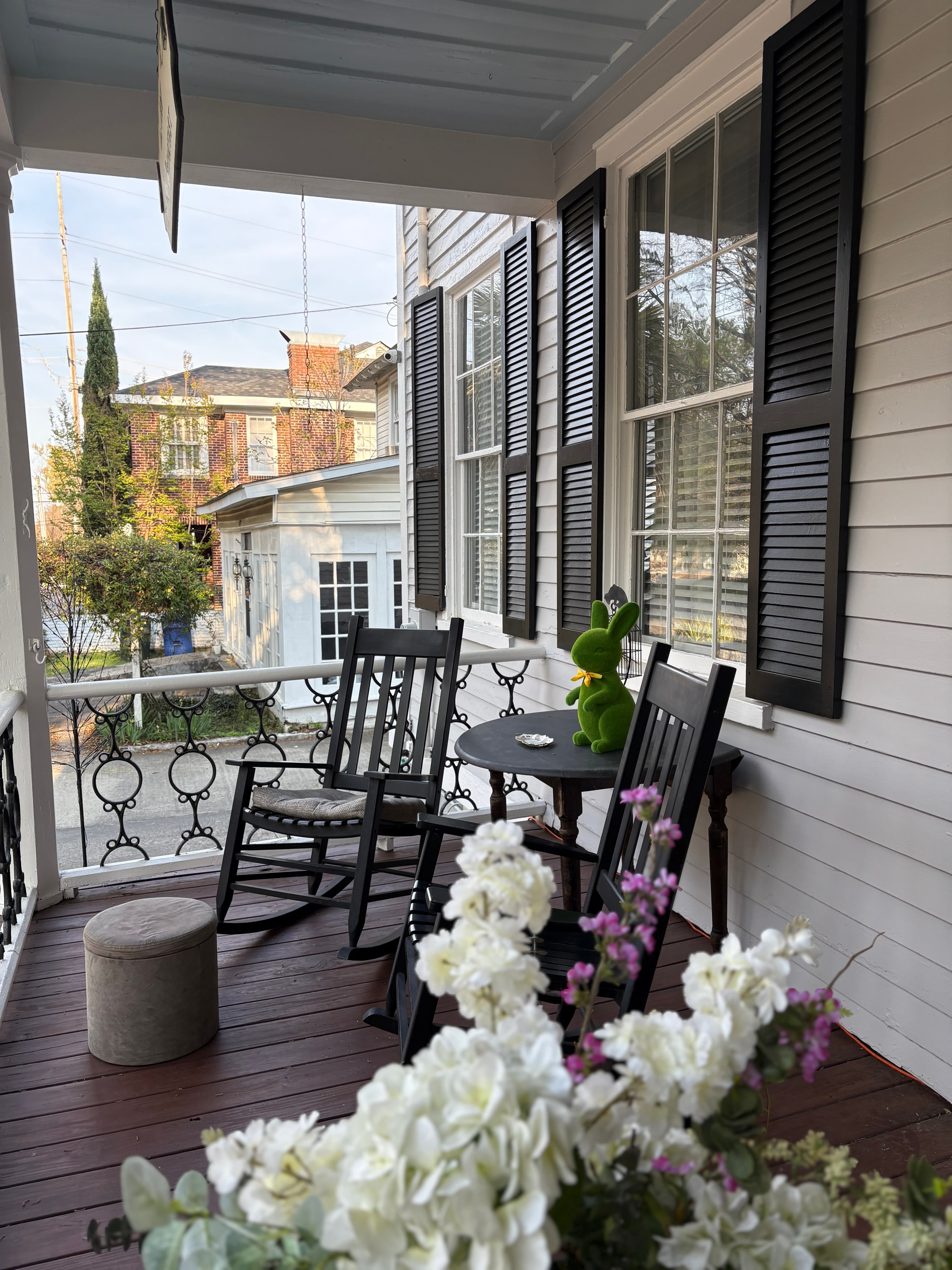 A cozy porch with rockers, a small table, and a green plush toy surrounded by flowers. A cozy porch with rockers, a small table, and a green plush toy surrounded by flowers.